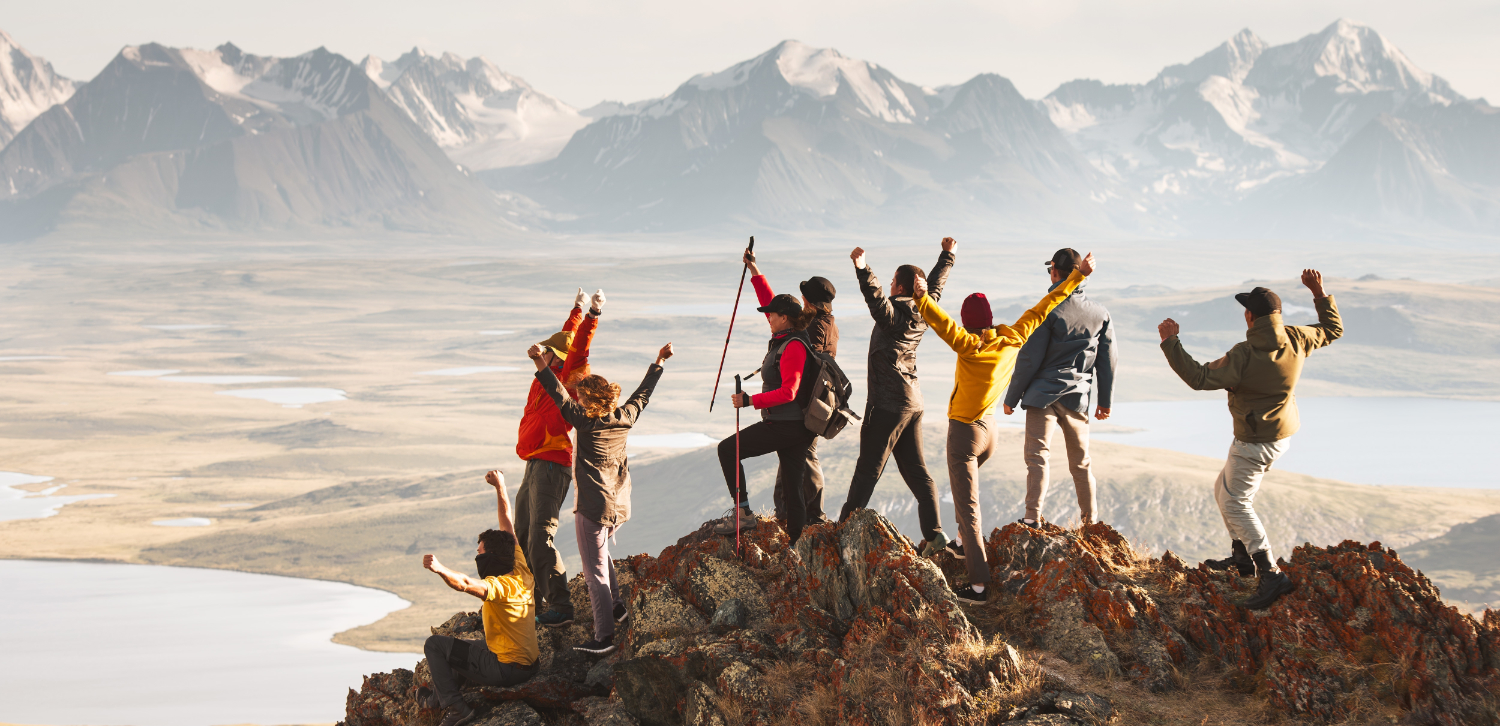 A large group of diverse tourists celebrates the completion of their climb to the top of the mountain with great view at sunset. Mixed ages and skills