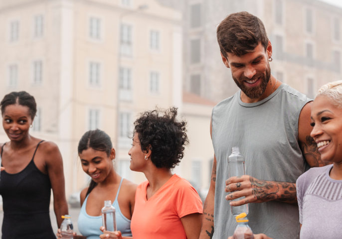 Group of smiling athletes is walking and drinking water after a workout session in a city setting, enjoying each other's company and the refreshing break