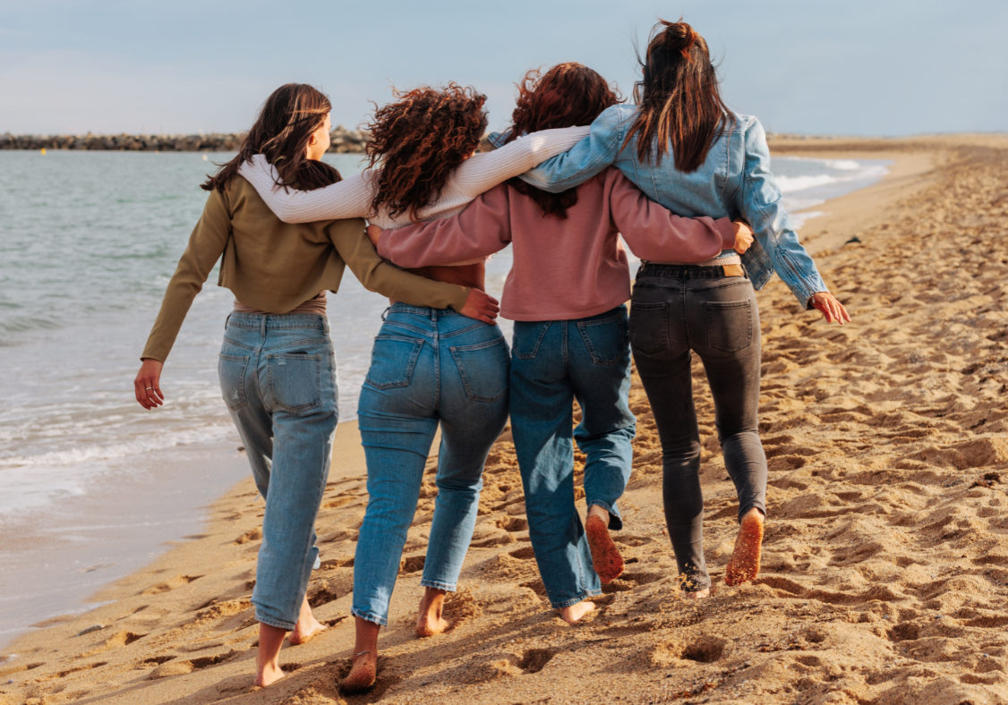 Rare view of  a four young women walking together barefoot on the beach